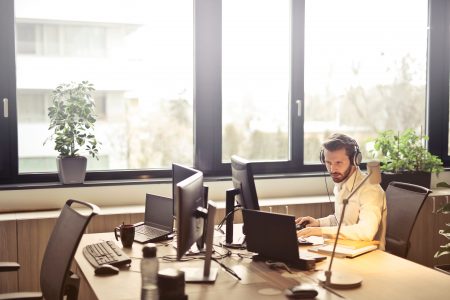 Man with headphones at desk with several computer monitors